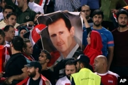 FILE - Syrian soccer fans hold a poster of their president, Bashar al-Assad, before a match with Iran, at Azadi Stadium, in Tehran, Iran, Sept. 5, 2017.