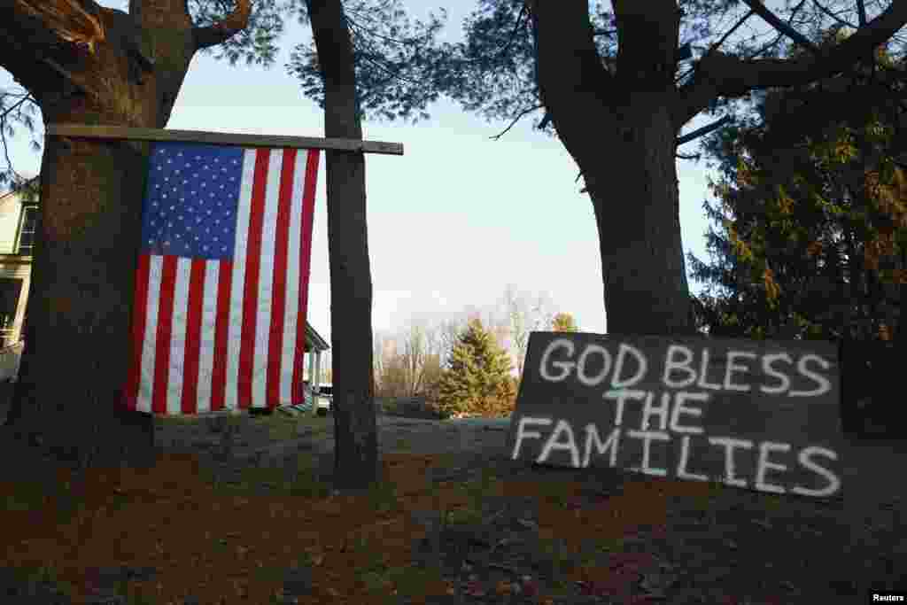 12月15日，康州纽敦桑迪.胡克小学附近挂着一面美国国旗,树边靠着的标语牌上写着:愿神祝福各个家庭。