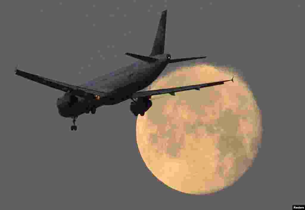 A passenger plane flies past the moon on its final descent to Heathrow Airport in London, Britain.