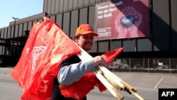 A steelworker carrying flags by German metalworkers' union IG Metall walks past a banner reading "Our future has a heart of steel" during a protest of steelworkers against European policies on April 11, 2016 in Duisburg, western Germany.