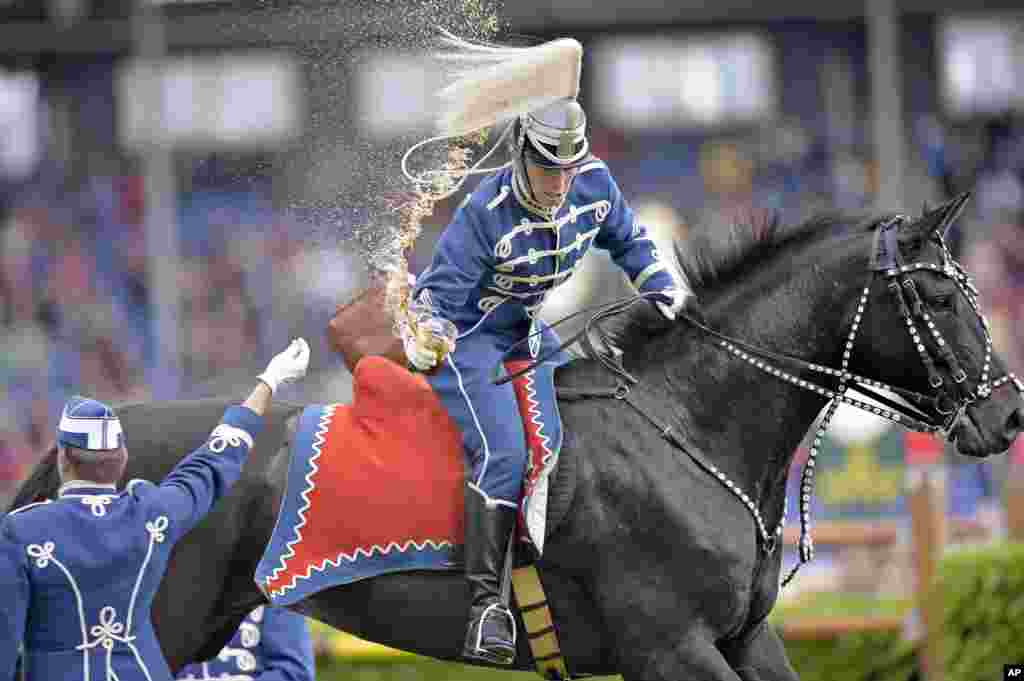 A Danish Guard hussar snatches a drink seated on a galloping horse during the opening ceremony of the CHIO Equestrian Festival in Aachen, Germany. 