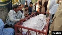 FILE - Relatives sit beside the body of what they say is a female polio vaccinator who was killed by unidentified gunman, as they protest in front of the district commissioner office in Chaman, Pakistan, Apr. 25, 2019.