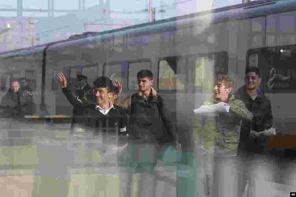 Six young men, one Syrian and five Afghans, wave on the platform of the Calais train station, northern France, as they leave for Britain.