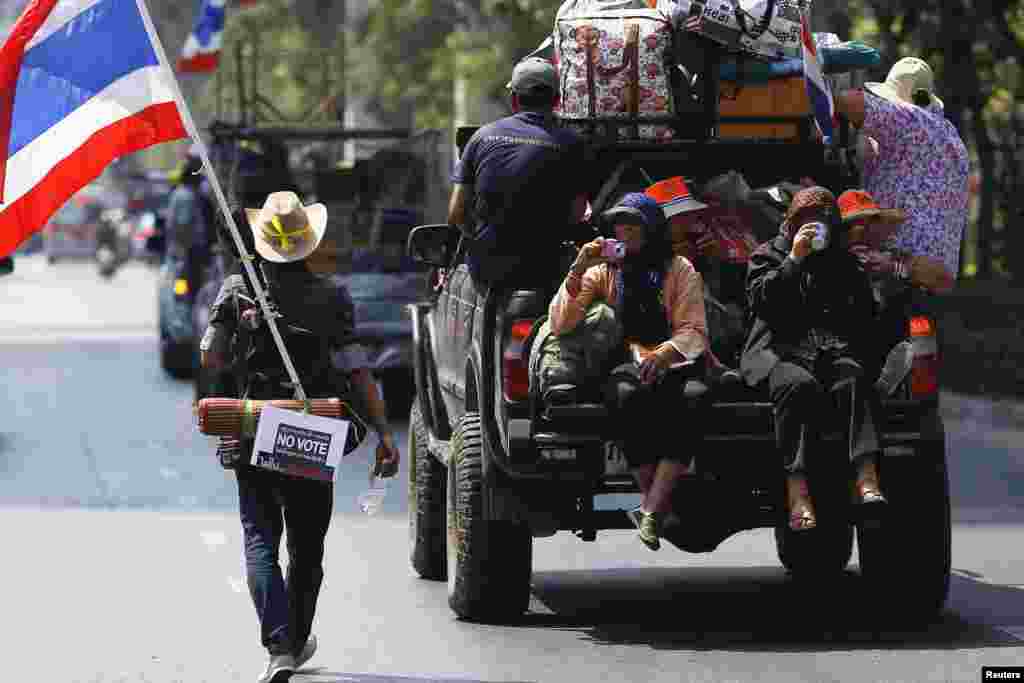 An anti-government protester carrying a national flag, a guitar and a "No Vote" sign follows others moving from one protest camp to another in Bangkok Feb. 3, 2014.