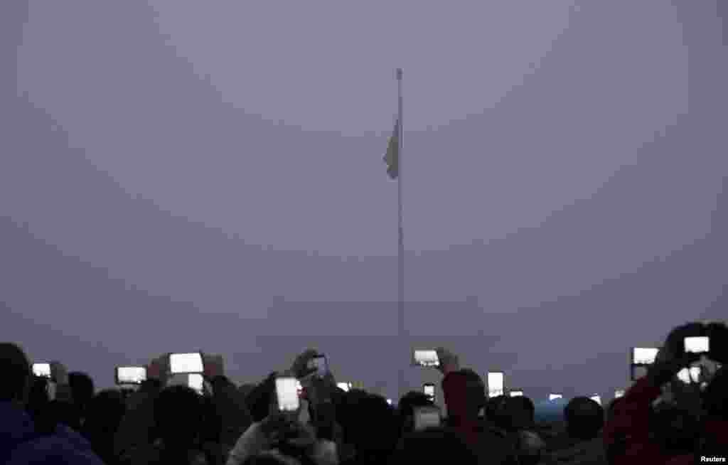 Khách tham quan dùng điện thoại di động chụp hình và quay video lễ kéo cờ tại Quảng trường Thiên An Môn giữa khói mù dày đặc ở Bắc Kinh, Trung Quốc.
