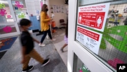 Students walk past a social distancing reminder sign while heading to the nurse's office to be tested for COVID-19. (AP Photo/Charles Krupa)