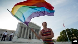 Gay rights advocate Vin Testa waves a rainbow flag in front of the Supreme Court at sun up in Washington, June 26, 2013. 