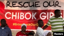 Protesters from the remote town of Chibok stand next to a poster reading "Rescue our Chibok girls," at a protest calling for the release of abducted schoolgirls, in Abuja, Nigeria, May 16, 2014.