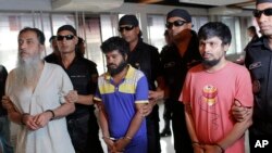 Các thành viên của Đội Hành động Bangladesh trong trang phục màu đen đứng sau các nghi can bị bắt giữ: Ansarullah Bangla Team, Touhidur Rahman, thứ hai bên trái, Sadek Ali, giữa và Aminul Mollick tại Dhaka, ngày 18/8/2015.