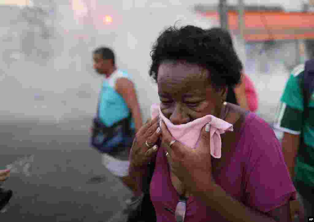 A senhora cobre a cara para proteger-se do gás usado pela polícia durante o protesto contra o aumento das tarifas de autocarro no Rio de Janeiro, Fev. 6, 2014.