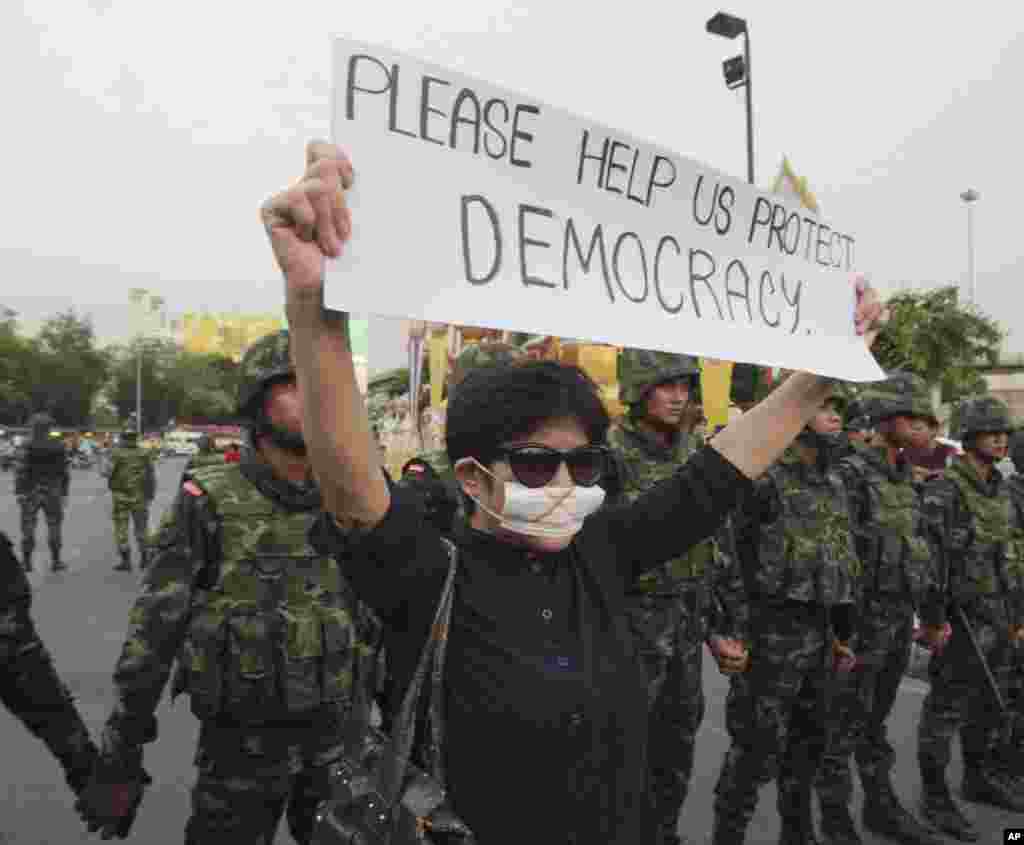 An anti-coup protester holds a banner in front of soldiers during a demonstration at the Victory Monument in Bangkok, May 26, 2014.