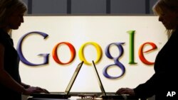 FILE - Exhibitors work on laptop computers in front of an illuminated sign of the Google logo in Hanover, Germany, April 17, 2007. Google is abandoning plans to establish a campus for tech startups in Berlin.