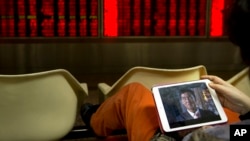 A Chinese investor watches a video on a tablet computer while monitoring stock prices in a brokerage house in Beijing, Jan. 29, 2016.