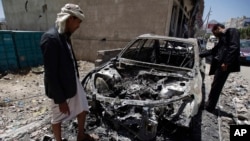 Men look at a car destroyed by a recent Saudi-led airstrike in Yemen's capital, Sana'a, April 25, 2015. 