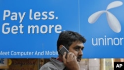 A man speaks on a mobile phone in front of a billboard of Uninor at a market in Ahmedabad, February 6, 2012. Telenor's joint venture with Unitech, which operates under the Uninor brand, has been among the most aggressive of India's newer telecoms compani
