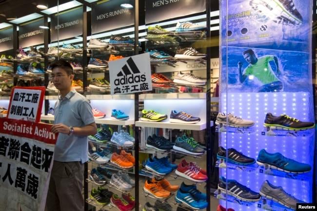 A labor activist stands outside an Adidas store with a protest sign, in support of a strike by workers of Yue Yuen Industrial Holdings, pasted on its shop window during International Labour Day in Hong Kong May 1, 2014.