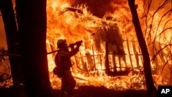 FILE - A firefighter sprays water as flames from the Camp Fire consume a home in Magalia, Calif., Nov. 9, 2018. A new federal report warns that extreme weather disasters are worsening in the U.S. The report, issued Nov. 23, also frequently contradicts President Donald Trump.