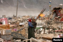 چین کے تبتی علاقے گیگو میں ایک خاتون ملبے کے ڈھیر پر اپنے بچنے کو اٹھائے حسرت سے اپنا گھر دیکھ رہی ہے۔ 19 اپریل 2010