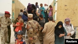 Serdadu Irak membantu warga sipil yang mengungsi dari Fallujah akibat kekejaman Islamic State, selama terjadinya badai pasir. Pinggiran Fallujah, Irak.