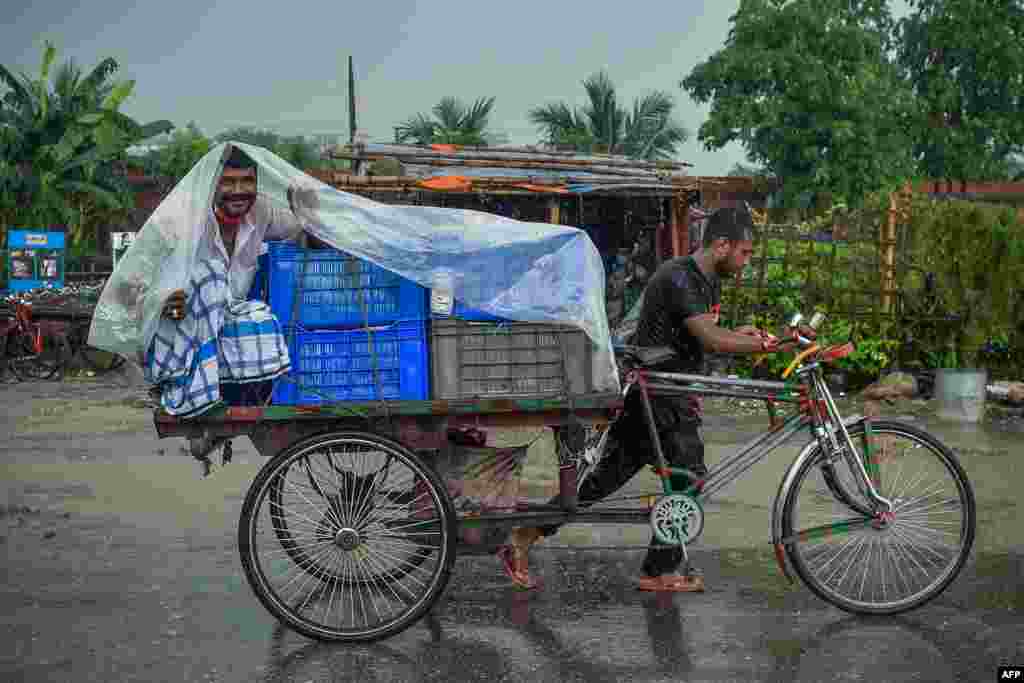 A man wraps a plastic sheet to shelter from the rain while sitting on a cycle-rickshaw cart in Dhaka, Banglaesh.