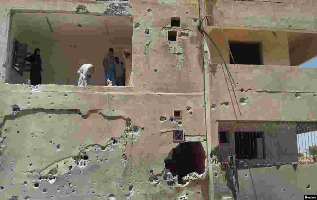 People stand on a building damaged by what activists said was shelling by forces loyal to Syrian President Bashar al-Assad in Raqqa province, eastern Syria June 26, 2014. 