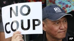 A Thai anti-coup protester holds a banner during a protest outside a shopping complex in Bangkok, Thailand Saturday, May 24, 2014. Thailand's coup leaders said Saturday that they would keep former Prime Minister Yingluck Shinawatra, Cabinet members and an