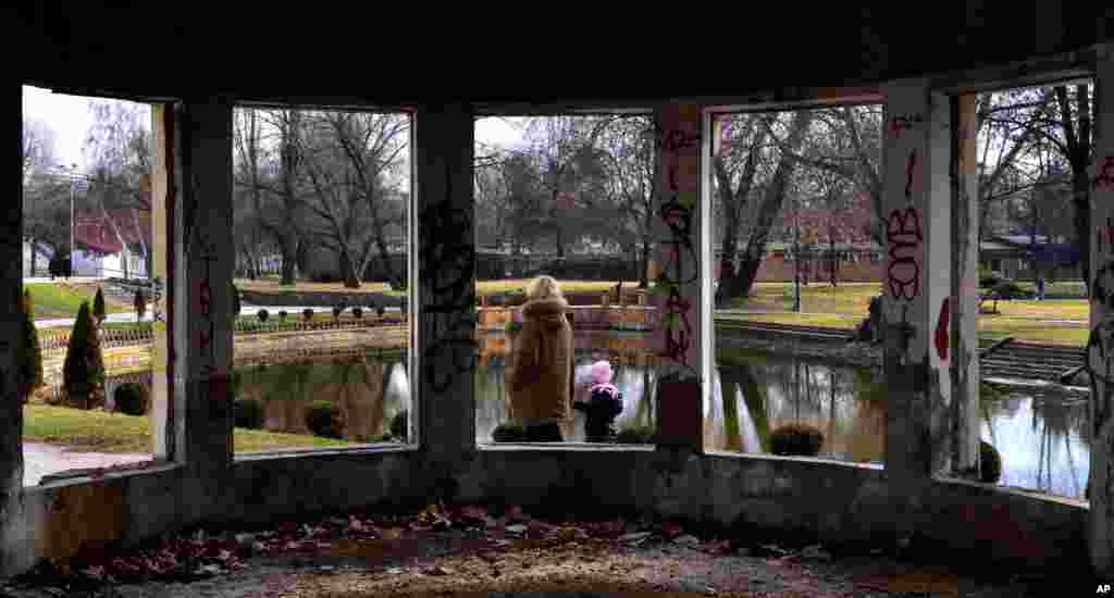 A woman with a child passes by the ruins of an abandoned restaurant in a park in Skopje, Macedonia.