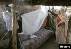 FILE - A Sudanese women gets help setting up a bed net.
