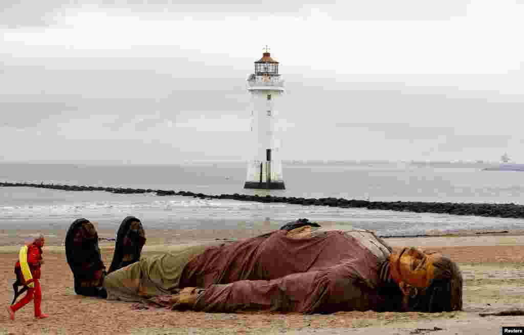 A lifeguard passes one of Royal Deluxe&#39;s giant marionette puppets as it lies on the beach at New Brighton, Britain.