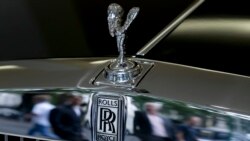FILE - Pedestrians are reflected in the chrome work under the Spirit of Ecstasy on the front of a Rolls- Royce car, in a show room in London, July 8, 2014.