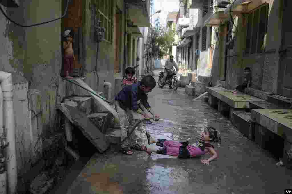 Children play with a water pipe to cool off on a street during hot summer in Rawalpindi, Pakistan.