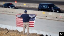 Dejvid Morgan na Hajlends ranču, Kolorado, drži američku zastavu dok vozila pripadnika snaga reda prevoze telo ubijenog zamenika šerifa, ubijenog tokom intervencije povodom prijavljenog porodićnog nasilja, 31. decembra 2017. u Hajlends Ranču, Kolorado.