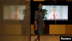 Seorang perempuan dengan masker wajah berjalan melewati layar yang menunjukkan siaran Perdana Menteri Singapura Lee Hsien Loong membahas wabah Covid-19, di kawasan pusat bisnis di Singapura, 3 April 2020. (Foto: REUTERS)