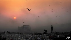 FILE- A thick blanket of smoke is seen against the setting sun as young ragpickers search for reusable material at a garbage dump in New Delhi, India.