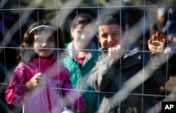 FILE - Children behind a fence in a temporary holding center for migrants near the border line between Serbia and Hungary in Roszke, southern Hungary in Roszke, Sept. 12, 2015.