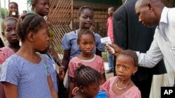 FILE - In this Jan. 19, 2015 photo, a health care worker, right, takes the temperatures of school children for signs of the Ebola virus before they enter their school in the city of Conakry, Guinea. 