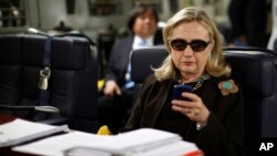 FILE - In this Oct. 18, 2011, photo, then-secretary of state Hillary Clinton checks her smartphone aboard a C-17 military plane en route to Tripoli, Libya. Clinton's handling of emails has figured prominently in the presidential campaign.