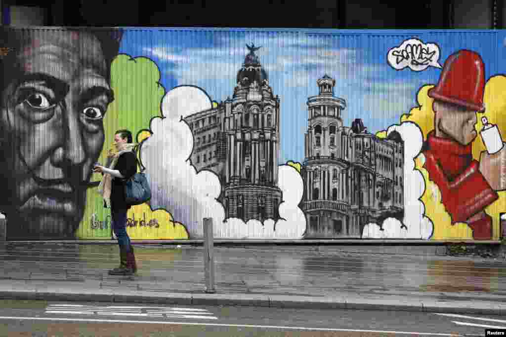 A woman smokes beside a barrier that is decorated with artwork in central Madrid, Spain.