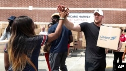 FILE - In this Sept. 3, 2017, file photo, Anna Ucheomumu, left, high fives Houston Texans defensive end J.J. Watt after loading a car with relief supplies to people impacted by Hurricane Harvey, in Houston. J.J. Watt is being honored by the NFL Players Association after raising more than $29 million for Hurricane Harvey relief efforts.