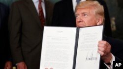 President Donald Trump holds up a signed memorandum calling for a trade investigation of China, Aug. 14, 2017, in the Diplomatic Reception Room of the White House in Washington.