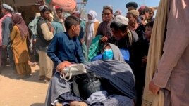 A porter pushes a wheelbarrow carrying an elderly Afghan woman with her family as they enter into Pakistan from Afghanistan at a border crossing, in Chaman, Pakistan, Thursday, Aug. 19, 2021.