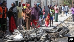 Somalis stand over the wreckage of car bomb which exploded outside a restaurant in Mogadishu, Somalia, April , 21, 2015.