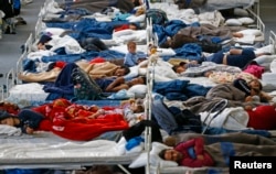 Migrants rest on beds at an improvised temporary shelter in a sports hall in Hanau, Germany, Sept. 22, 2015.