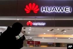 FILE - A man lights a cigarette outside a Huawei retail shop in Beijing, Dec. 6, 2018.