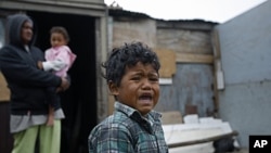 A boy reacts, in front of a house in a township on the outskirts of Cape Town, South Africa. Thousands of South Africans live without running water in their houses and without electricity. (2010 file photo)