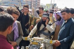Pejuang Taliban (tengah) dikelilingi oleh penduduk setempat di Pul-e-Khumri setelah Taliban merebut Pul-e-Khumri, ibu kota provinsi Baghlan sekitar 200 km sebelah utara Kabul, 11 Agustus 2021. (AFP)