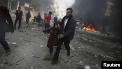 A man holds the hand of a girl as they rush away from a site hit by what activists said were airstrikes by forces loyal to Syria's President Bashar al-Assad, in the Douma, Syria, Nov. 7, 2015.