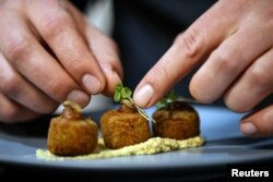 Chef Mario Barnard meletakkan daun ketumbar di atas kroket yang dibuat dari tepung Hermitia illucens atau larva lalat serdadu hitam dan kacang arab, yang disajikan dengan hummus dari cacing mopane di Restoran Insect Experience di Cape Town, Afrika Selatan