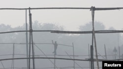 FILE - A laborer dismantles scaffolding near the India Gate war memorial on a smoggy day in New Delhi.