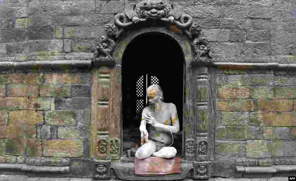 A Hindu sadhu - holy man - smears colored paste onto his body at the Pashupatinath Temple in Kathmandu, Nepal.